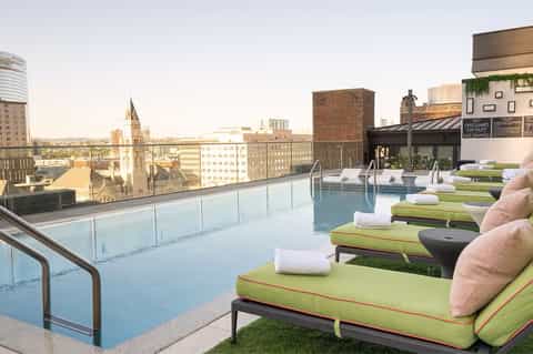 Rooftop pool with city skyline views, green lounges with cushions, and architectural landmarks