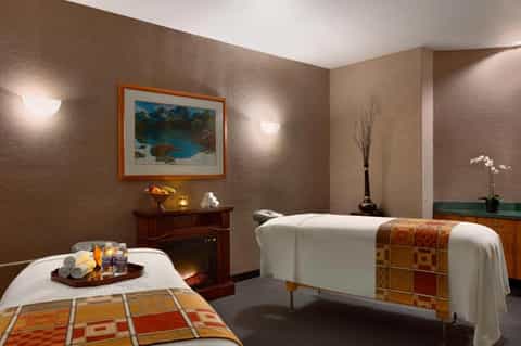 Spa treatment room with two massage beds, warm lighting, and decorative artwork