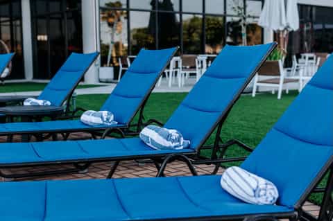 Row of blue chaise lounges with white rolled towels on manicured lawn facing modern building