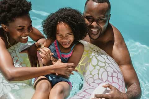 Family of three enjoying pool time together with inflatable floats in bright turquoise water