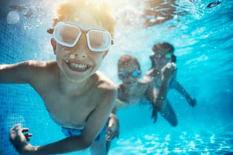 Child snorkeling underwater with goggles, smiling at camera