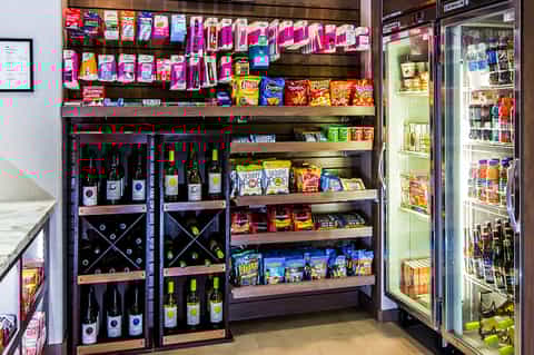 Retail shelf display with wine bottles, snacks, and beverages including a refrigerated cooler on the right