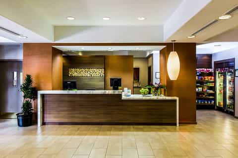 Hotel lobby with curved wooden reception desk, pendant lighting, and convenience store