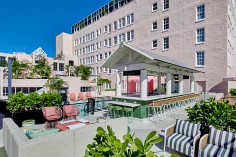 Modern rooftop bar and lounge area with pink seating, green accents, and pink umbrellas