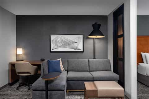 Modern hotel suite with gray sofa, desk, pendant lamp, and framed artwork on charcoal accent wall