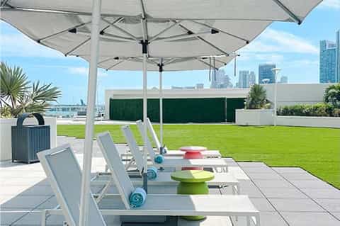 Rooftop terrace with white umbrellas, loungers, green lawn, and city skyline views