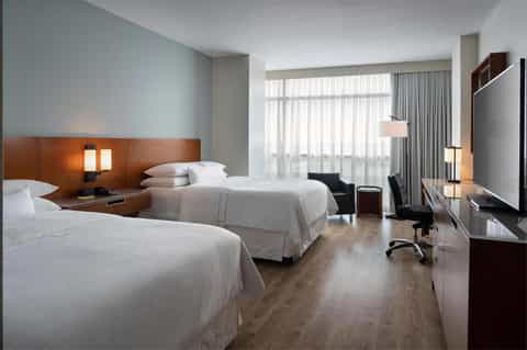 Spacious double hotel room with two queen beds, wooden headboard, work desk, and contemporary furnishings
