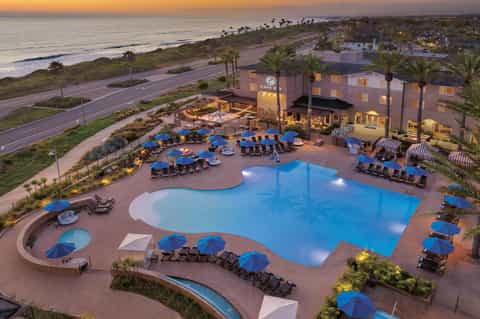 Aerial view of beachfront resort pool complex lit at dusk with blue umbrellas