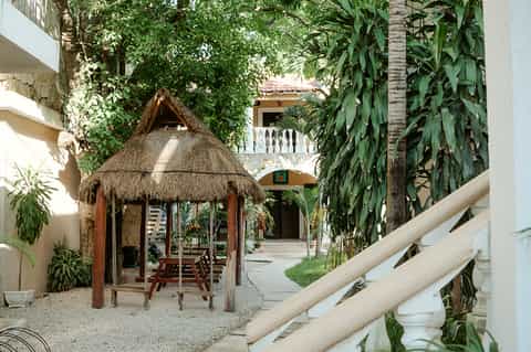 Tropical courtyard with thatched-roof gazebo, colonial architecture, and lush vegetation