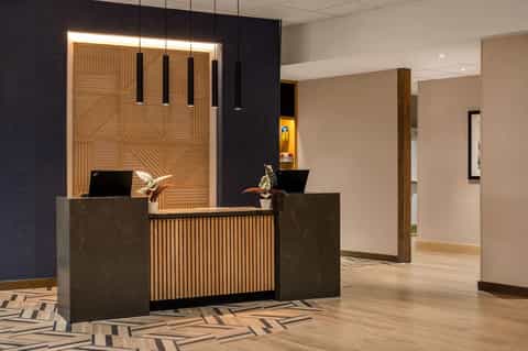 Contemporary hotel lobby featuring wooden accent wall, dark reception desk with pendant lighting