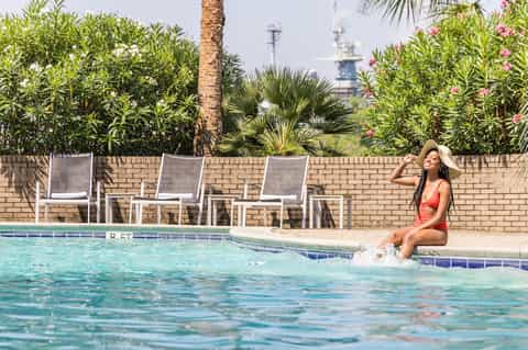 Woman in red swimsuit at pool edge with loungers and tropical plants along brick wall