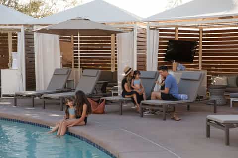 Resort pool area with family enjoying lounge chairs under pergola with umbrella and white curtains