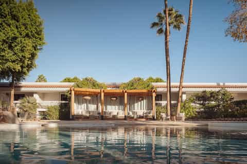 Resort pool with covered cabanas, palm trees, and Mediterranean-style architecture