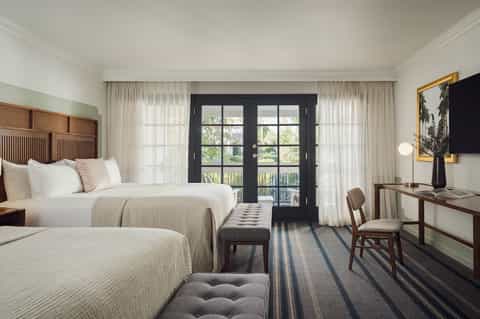 Hotel room with two queen beds, dark balcony doors, curtains, and mid-century modern furnishings