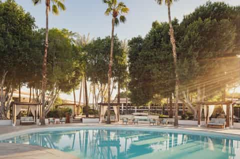 Resort pool surrounded by palm trees and lounge pavilions with ocean views at sunset