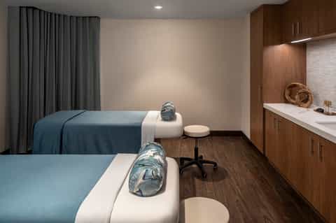 Modern spa treatment room with massage beds, dark wood cabinetry, and minimalist design