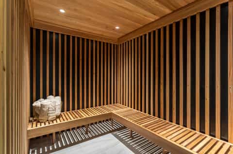 Modern sauna interior with wooden slat walls and benches, basket of white towels, recessed lighting