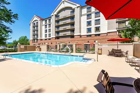 Outdoor swimming pool with red umbrellas, multi-story residential building, and landscaped patio area