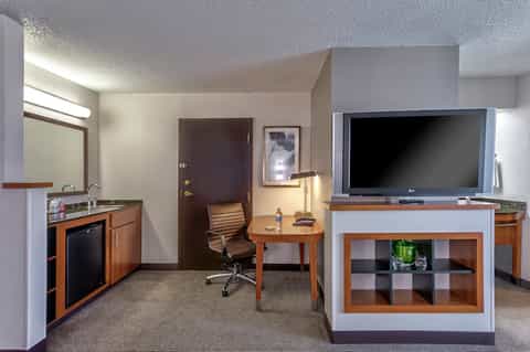 Hotel suite with kitchenette, desk area, TV, and wood furnishings