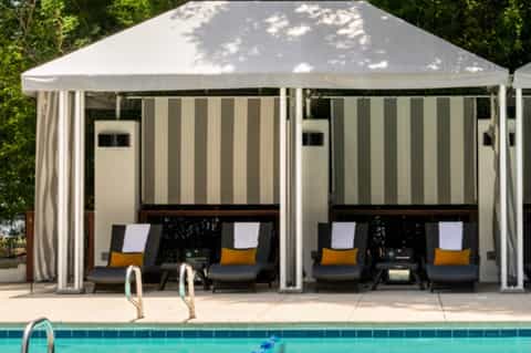 Two cabanas with cream canopies and lounge seating beside a swimming pool