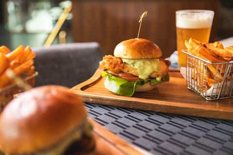 Gourmet burger and fries served on wooden board next to beer in an upscale restaurant setting