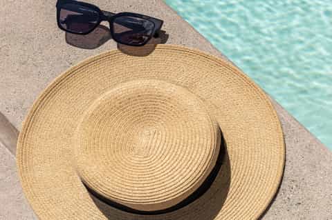 Straw hat and sunglasses on pool deck beside turquoise water on a sunny day