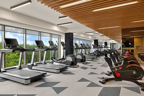 Bright fitness center with treadmills, exercise bikes, and wooden ceiling beams with city views
