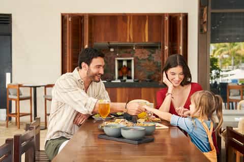 Family enjoying meal together at wooden dining table with kitchen and outdoor views in background