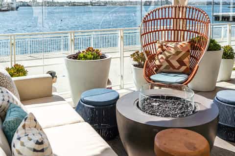 Waterfront balcony lounge with woven chair, fire pit, potted plants, and bay views