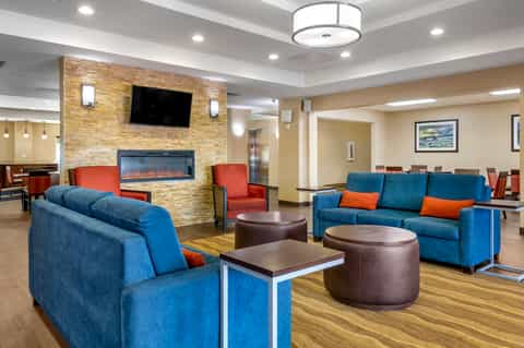 Modern hotel lobby lounge with blue sofas, orange accents, stone fireplace, and flat-screen TV