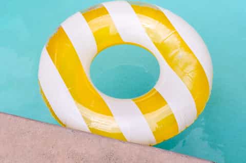 Yellow and white striped inflatable pool float resting on pool deck edge in turquoise water