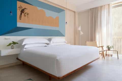 Modern hotel bedroom with blue accent wall, wooden bed frame, and ocean view balcony
