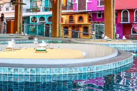 Poolside dining area with colorful buildings reflected in turquoise water features