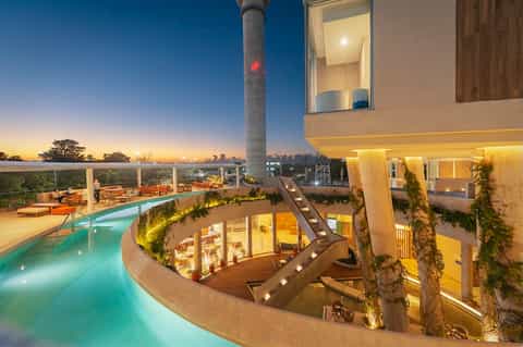 Illuminated multi-level modern resort with curved pools at dusk and city lights in background