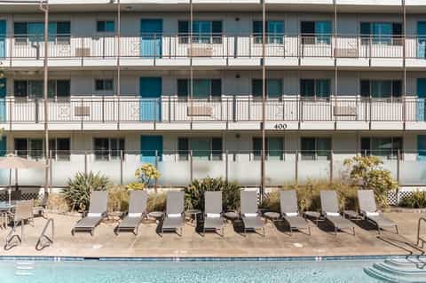 Multi-story beachfront resort building with white railings, pool, and lounge chairs below