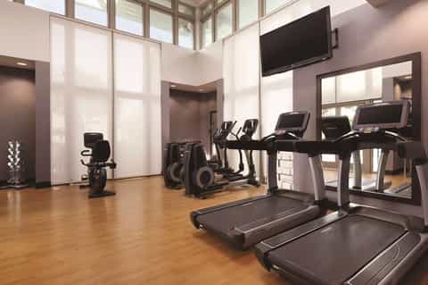 Modern fitness center with treadmills, exercise bikes, large mirrors, and floor-to-ceiling windows