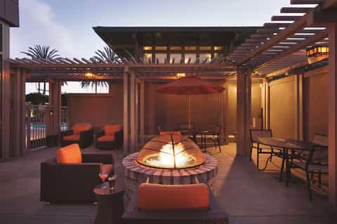 Upscale outdoor patio with fire pit, orange seating, wooden pergola, and ambient evening lighting