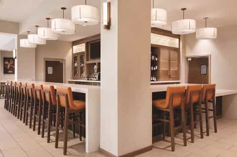 Modern hotel bar with wooden chairs, pendant lighting, and mirrored shelving