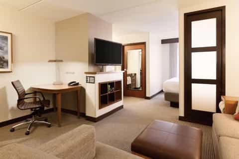 Modern hotel suite with work desk, TV, comfortable seating, and wood accents throughout
