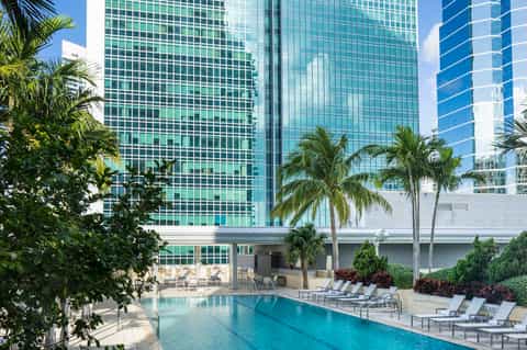 Resort pool surrounded by palm trees with modern glass high-rise hotel building in background