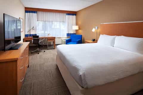 Hotel guestroom with queen bed, work desk, blue accent chair, and large windows with ocean view