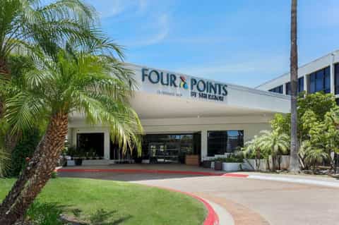 Four Points by Sheraton hotel entrance with modern signage, landscaping, and palm trees