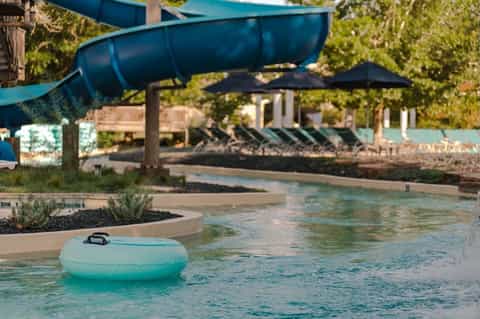 Blue water slide descending over a resort pool with lounge chairs and landscaping