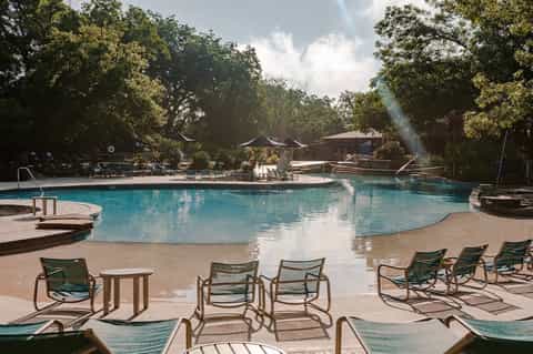 Resort pool surrounded by lounge chairs and trees, with wooden structures and open-air seating areas