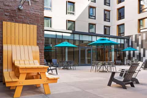 Outdoor courtyard with bold yellow Adirondack chair, turquoise umbrellas, and modern building facade