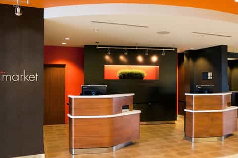 Modern hotel lobby reception area with orange and black accent walls, wooden curved desks, and ambient lighting