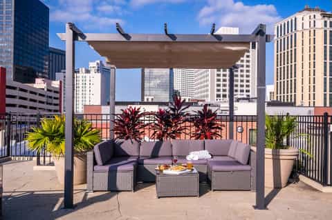 Rooftop terrace with pergola, gray sectional seating, tropical plants, city skyline view, and metal railings
