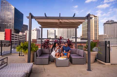 Urban rooftop lounge with pergola, modern seating, and city skyline views with tropical plants