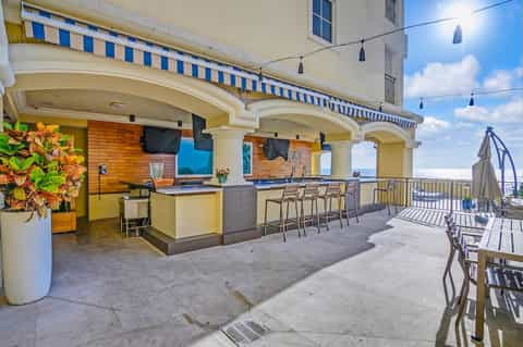 Rooftop bar and lounge with blue striped awning, yellow walls, ocean views, and casual seating