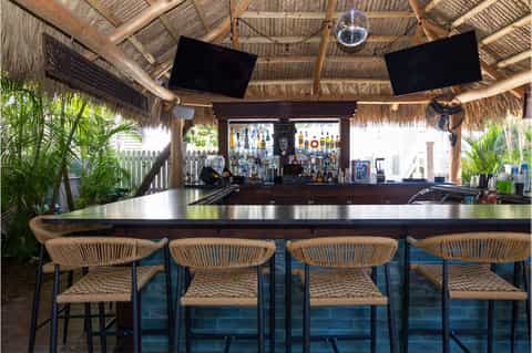 Tropical bar with thatched roof, woven seating, and waterfront views at dusk